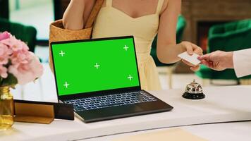 Laptop with greenscreen display on hotel front desk next to lounge area, modern isolated chromakey template at reception. Blank mockup copyspace screen on pc in tropical resort lobby. photo