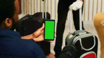 Travellers using greenscreen on phone, sitting in lounge area at hotel and looking at mockup copyspace. Couple waiting for registration procedure, holding smartphone with chromakey display. photo