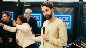 News reporter in crowded clothing store holding microphone and broadcasting black friday crazy behaviour. TV journalist creating live newscast on scene at local shopping center. photo