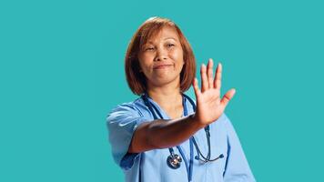 Close up shot of determined assertive nurse throwing stop hand sign, upset with work conditions. Firm BIPOC clinic employee doing halt gesturing, isolated over studio background photo