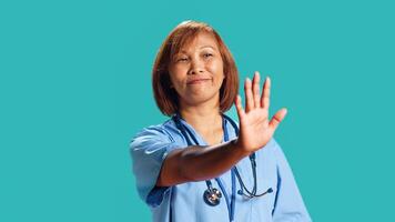 Close up shot of determined assertive nurse throwing stop hand sign, upset with work conditions. Firm BIPOC clinic employee doing halt gesturing, isolated over studio background photo