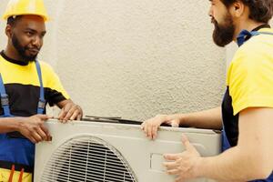 African american repairman and apprentice worker pulling apart old defective outdoor hvac system to replace it with new performant condenser after draining refrigerant and replacing ductwork photo