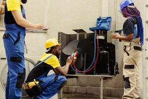 Adept repairman expertly refilling freon in HVAC system while using benchmarking tools to precisely measure the pressure in air conditioner, ensuring optimal cooling performance photo