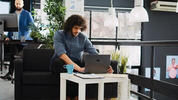 Employee reviews statistics on laptop while he works on development strategy online, AI developer. Professional analyst looking at marketing information reports, unicorn business open space. photo