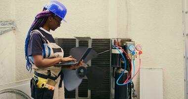 Adept african american repairman working on outside air conditioner holding laptop. Proficient worker optimizing HVAC system performance, ensuring it operates at maximum capacity photo