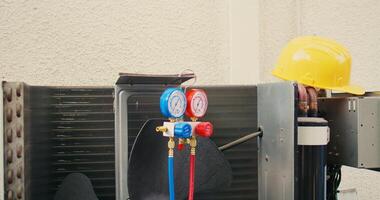 Close up of safety hardhat and pressure measurement device used for checking HVAC system refrigerant in need of maintenance. Set of freon levels benchmarking tool mounted on air conditioner photo