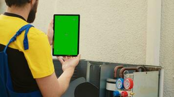 Mechanic ordering new components on green screen mock up tablet for out of order air conditioner after finishing troubleshooting. Expert looking online for hvac system replacement parts photo