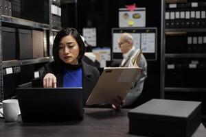 Asian manager accountant checking annual profit revenue paperwork before business consulting meeting. Bureaucratic workplace filled with flowcharts and file folders on shelves photo