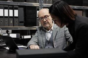 Professional accountancy executives imputing bookkeeping administrative data paperwork on laptop. Bureaucracy archival cabinet room filled with folders and diagram charts photo