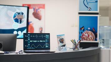 Cardiology diagnosis on laptop at desk, showing cardiogram and heart rate in empty medical facility waiting area. Electrocardiogram analysis and heartbeat pressure on display in lobby. photo