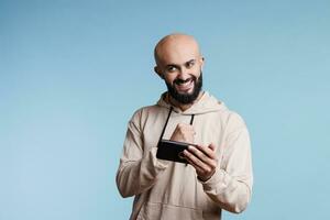 Excited happy arab gamer winning mobile phone game and celebrating victory. Cheerful young man showing winner gesture with fist while playing online videogame on smartphone photo