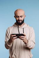 Arab man using smartphone application and playing video game during leisure activity. Young smiling person holding mobile phone in vertical mode and watching video online photo