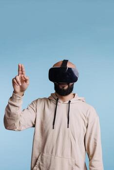 Man wearing vr headseat while playing virtual reality game and gesturing with two fingers. Young person enjoying metaverse and cyberspace simulation exploration experience photo