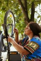 joven activo hembra ciclista avaro un llave inglesa para apretar empulgueras y servicio bicicleta partes afuera. deportivo entusiasta africano americano mujer participación profesional herramienta para bicicleta mantenimiento en foto