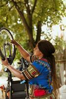 Fit and active african american female cyclist fastening bike tire safely for outside cycling. Dedicated black woman performing bike maintenance skillfully fixing bicycle wheel with wrench as photo