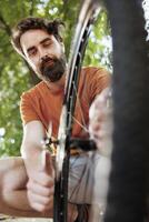 Committed healthy and active man outdoor showing dedication in adjusting and securing bicycle parts for recreational summer cycling. Image showing young man fixing bike wheel, summer activity. photo