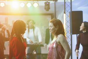 Young women doing dance battle at disco party with live electronic music in nightclub. Serious dancers standing on crowded dancefloor and improvising moves at discotheque photo