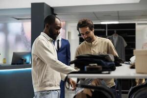 Clothing store shopper and assistant having conversation about fashion trends while exploring apparel rack. African american man asking boutique worker for help in choosing outfit photo