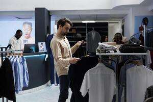 Young caucasian man checking tie and shirt match while choosing formal outfit in clothing store. Customer examining apparel and accessory style while shopping for menswear in boutique photo