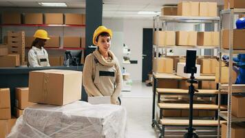 Young adult filming advertisement video in stockroom, showing products boxes on online social media page. Storage room workers using mobile phone to record PR ad, industrial goods. photo