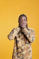 Young adult covering mouth with palms, doing doing three wise monkeys symbolic sign, standing in studio over yellow background. African american man showing silence gesture, not speaking concept photo