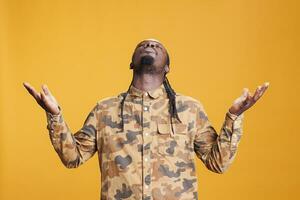 African american prayer standing with palms faced to sky, asking god for forgiveness in studio over yellow background. African american religious man showing gratitude, praying to jesus photo