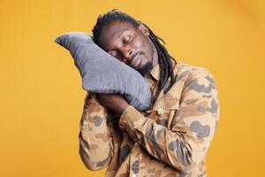 retrato de joven adulto participación almohada a tomar un siesta en estudio, cómodo actitud a dormir y descansar. africano americano hombre con ojos cerrado molesto a reparar durmiendo calendario con hora de acostarse hora. foto