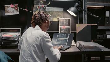 Female inspector reading crime case file in archive, trying to conduct investigation. African american woman analyzing surveillance photos for clues, uncovering new crime details.