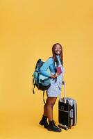 African american girl enjoying holiday trip with passport, carrying trolley bags luggage in studio. Young woman tourist travelling on urban adventure, weekend getaway with id documentation. photo