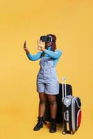 Modern girl using vr headset on holiday, carrying suitcase bags and using virtual reality glasses. Young tourist having fun with artificial intelligence 3d goggles, travelling on vacation. photo