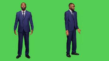 Young businessman expressing i dont know sign in studio and posing over full body green screen. Male company manager wearing office suit feeling confused, being uncertain or unsure on camera. photo