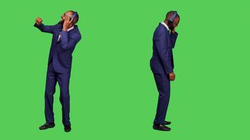 Office worker using headphones listening to music in studio, having fun with mp3 songs over full body greenscreen backdrop. Startup manager in suit dancing and wearing audio headset. photo