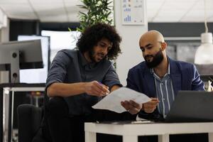 Two startup coworkers collaborating on business plan and analyzing sales report in coworking space. Company employees checking financial analytics and discussing market research photo