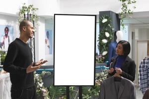 Clothing store worker and client discussing clothing brand collection while standing near ads whiteboard mockup. Boutique consultant using digital display to show apparel options to customer photo