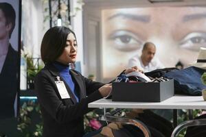 Smiling asian woman seller managing clothing store, checking accessory on garment display shelf. Department shopping center boutique assistant examining ties and belts for sale photo