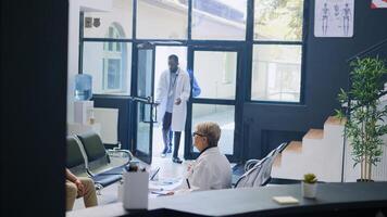 Senior man having checkup visit consultation in hospital waiting area, filling medical documents. Elderly patient discussing health care treatment with physician medic in lobby. Medicine concept photo