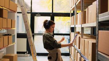 Woman dancing holding inventory list in storage room, having fun in depot and listening to music. Happy worker examining stock logistics with goods, looking at boxes on warehouse racks. photo