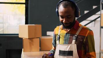 Worker listening to music in warehouse trying to check merchandise stock on shelves for retail store delivery. Male manager having fun dancing in storage room, inventory list. photo