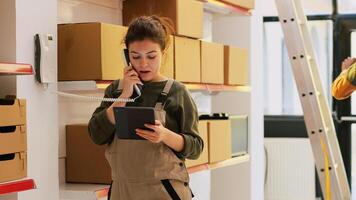 Manager talking to someone in storehouse, answering landline phone call to discuss with dispatcher about cargo distribution and production. Female supervisor inspecting merchandise. photo