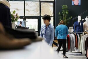 Manager preparing store for opening, arranging stylish clothes for customers in modern boutique. Shopping centre employee checking fashionable merchandise, working with trendy items photo