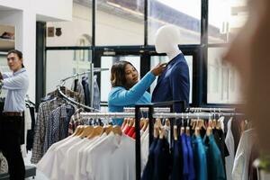 African american woman wanting to buy formal wear, looking at fashionable suit in clothing store. Stylish customer shopping for trendy merchandise, analyzing clothes fabric in modern boutique photo