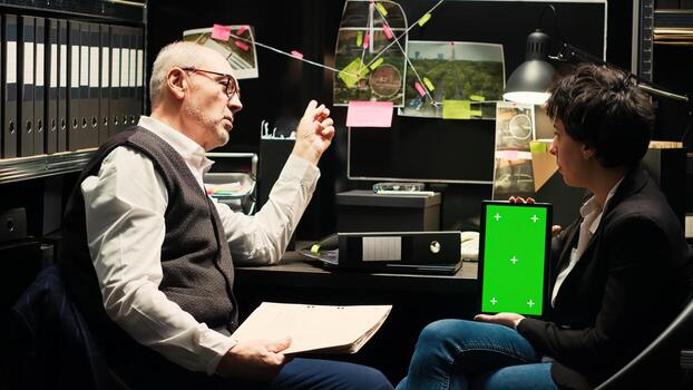 Detectives evaluate greenscreen display to try and solve criminal case, using chromakey tablet in police archive. Team of agents discussing strategy with isolated screen, catch culprit. photo