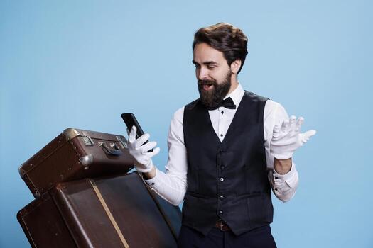 Outstanding hotel worker communicates with guests and surfing web pages while he reads encouraging news over studio backdrop. Professional doorman using online network for reservations. photo