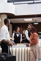 Asian worker registering guests in lobby at front desk, using computer and check in files for room reservation. Hotel staff team greeting people and keeping records of bookings. photo