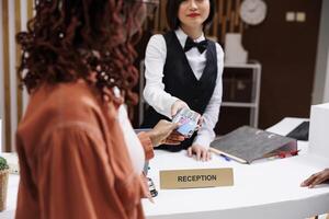 Young hotel guest paying for reservation at reception counter, using card at pos terminal. Front desk staff welcoming people at modern luxury resort, electronic payment at check in. photo