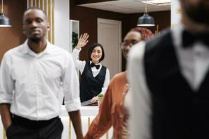 Happy receptionist waving at guests after doing check out process, wishing them a safe flight back home. Front desk employee saying goodbye to tourists after staying at luxury hotel. photo