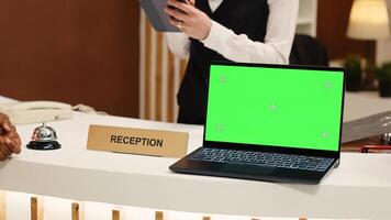 Close up of african american guest ringing service bell next to laptop chroma key green screen mock up at reception during check in process. Tourist ready to book in reservation at hotel front desk photo