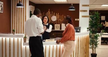 Friendly smiling asian receptionist handing contract on tablet for african american tourists to sign after upgrading room amenities. Happy relaxed guests on vacation trip checking in stylish hotel photo