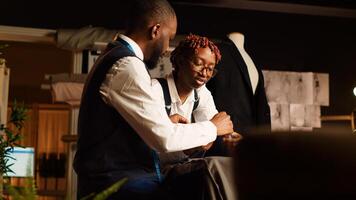 Designers reviewing material for items in atelier, choosing professional fabric on workstation before creating clothing line. Team of tailors manufacturing clothes with tools. Handheld shot. photo