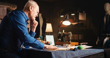 Man designer being under pressure, feeling frustrated about clothing items inspiration. Senior tailor trying to create luxury clothes, stressed craftsman failing to find perfect design. photo